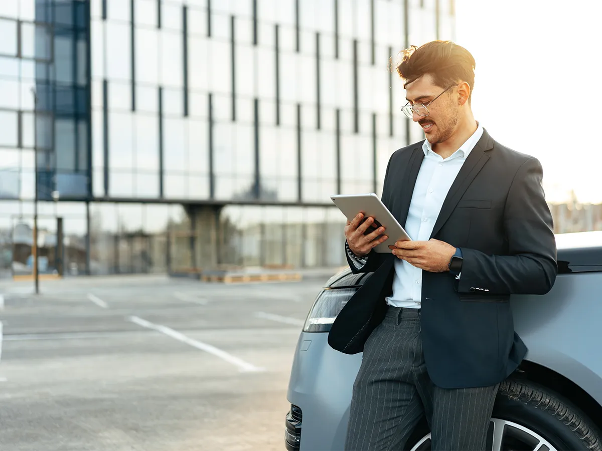 Antreprenor sprijinit de mașina firmei, analizând pe tabletă beneficiile fiscale ale leasingului auto